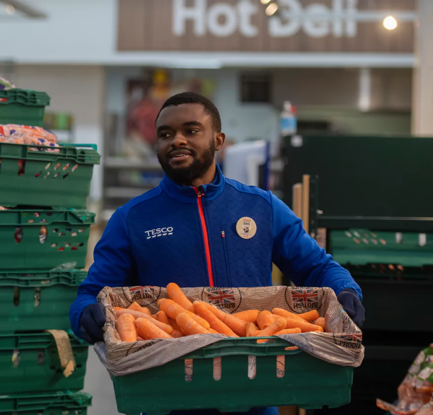 Colleague carrying a crate of carrots through a store